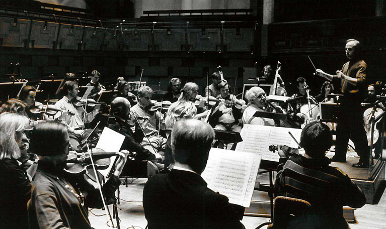 Stor orkester sedd från sidan. Gruppbild. Orkestern repeterar, Paavo Järvi dirigerar. Spelbild. Fotografi.