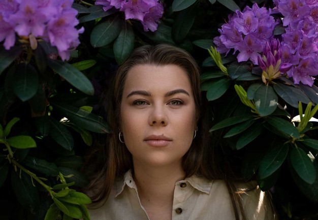 Woman standing among purple flowers. Looking into the camera. Photography.