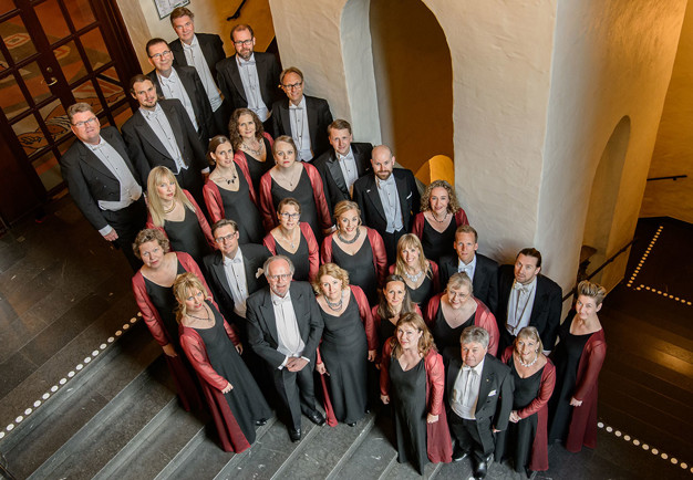 A choir in tails and evening dresses standing in the hall way. Photo.