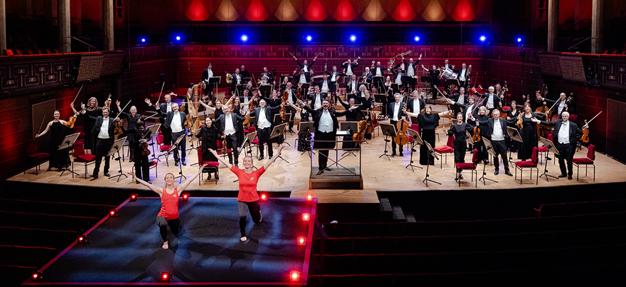 Två instruktörer som tränar framför en orkester. Fotografi.